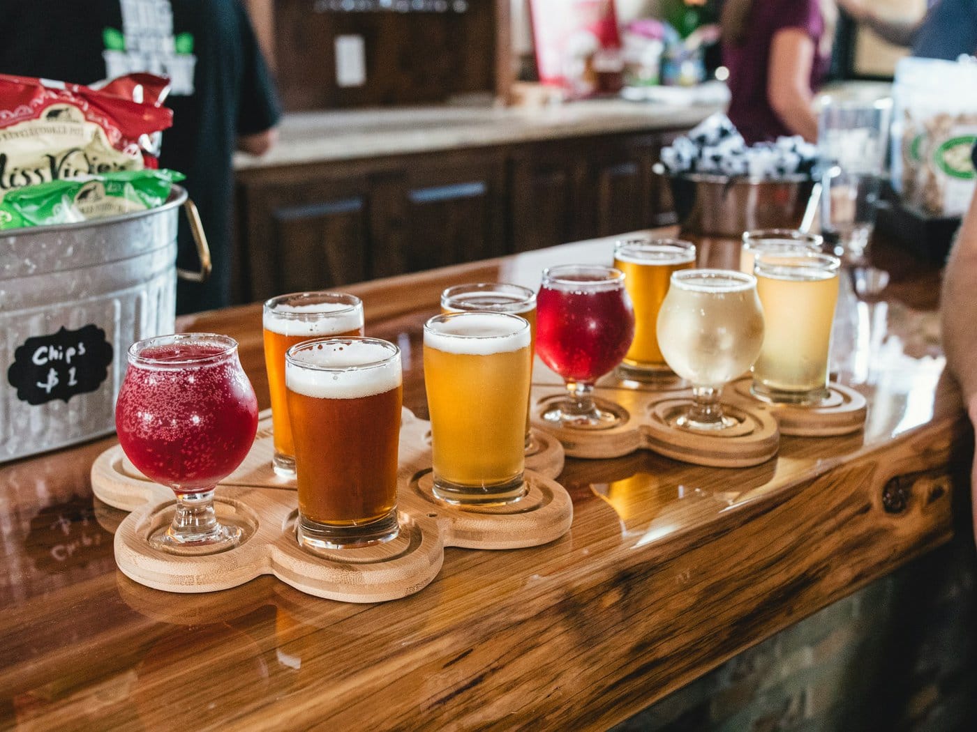 Various craft beers in glasses on wooden flight paddles arranged on a bar counter.