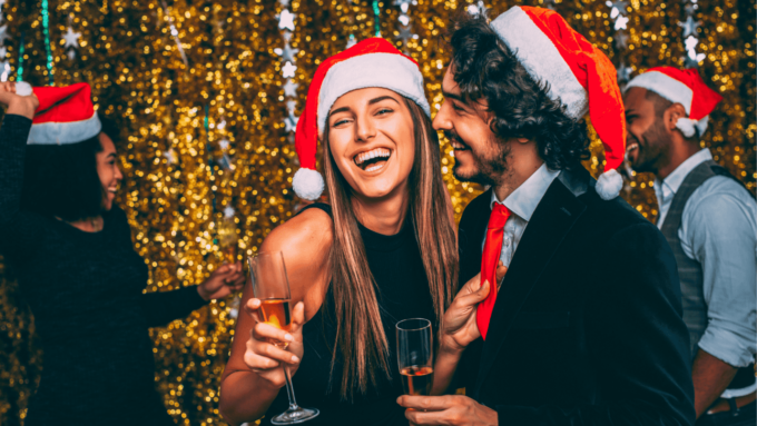 A Young Couple At A Christmas Party Hold Glasses Of Wine.