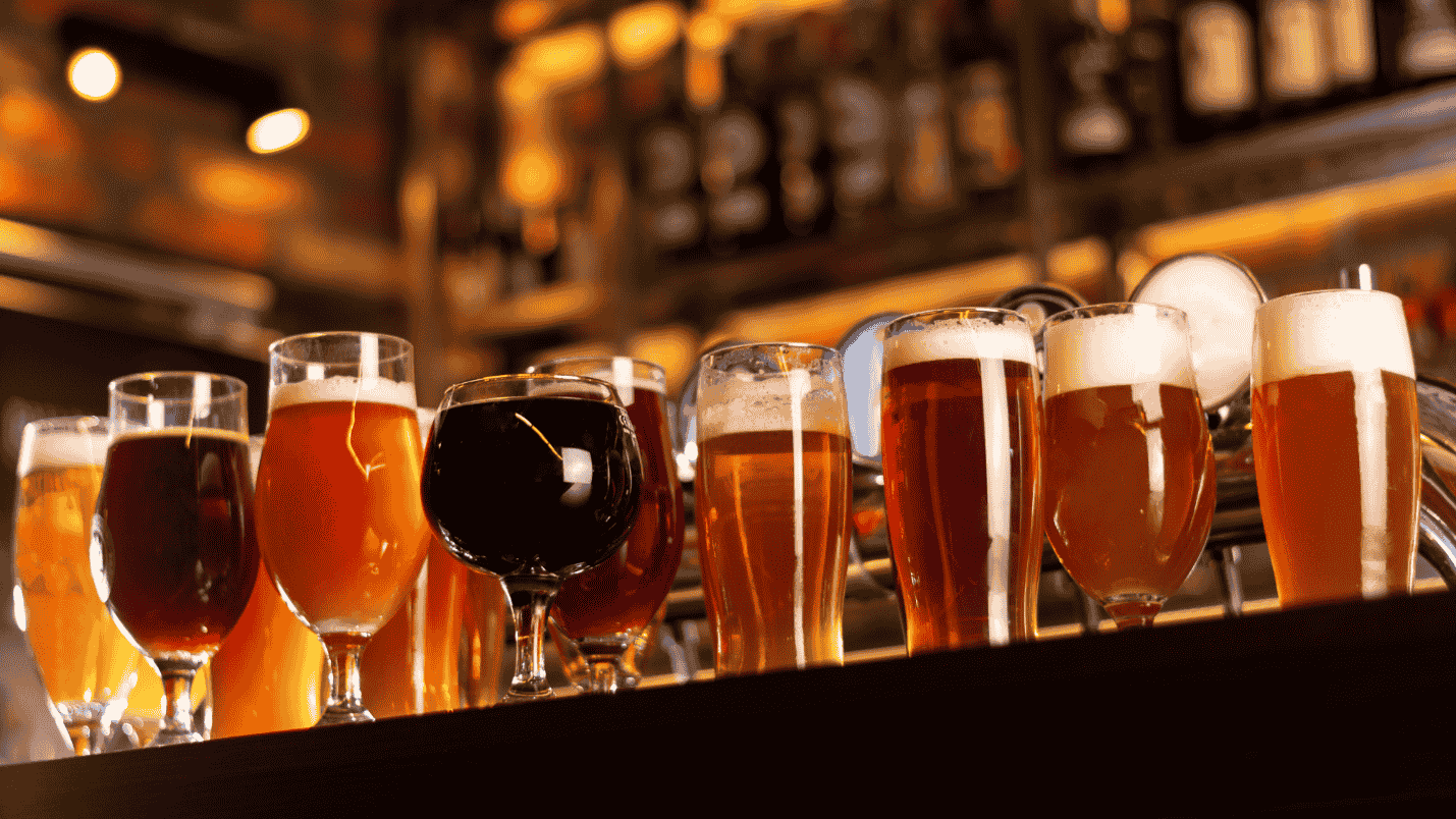 Various craft beverages in different shaped glasses sit on a bar.