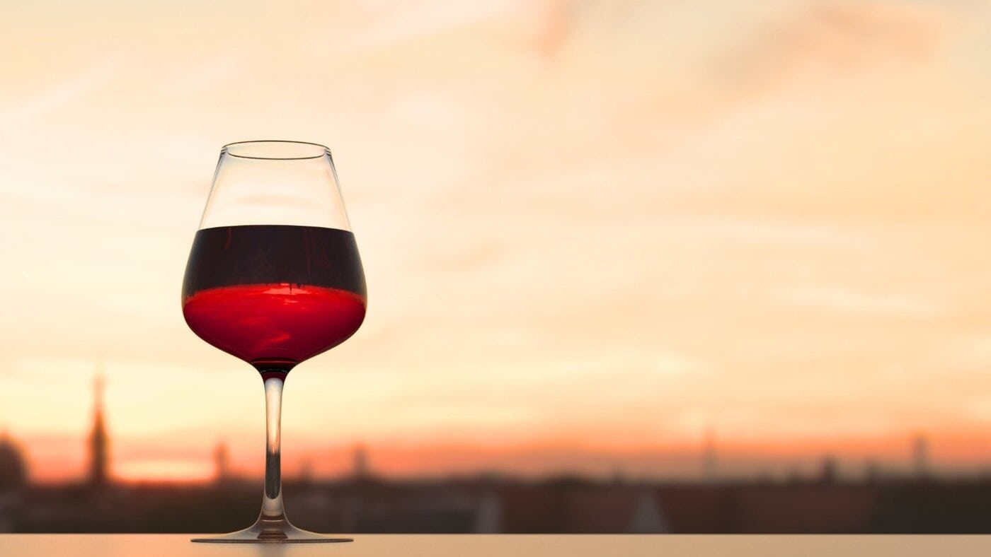A wine glass on a windowsill with a summer sunset behind it.