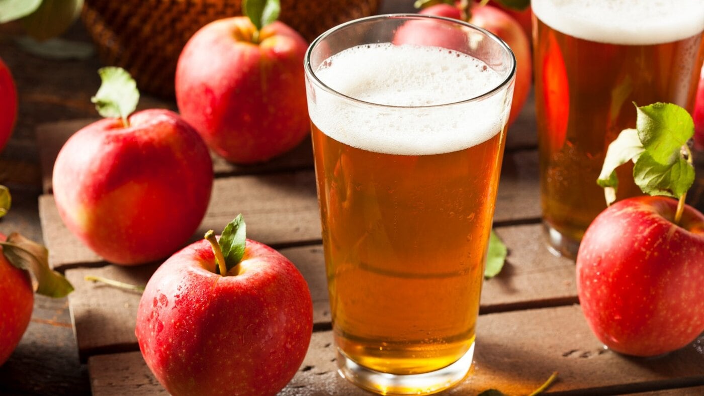 A glass pint of non-alcoholic cider next to fresh apples.