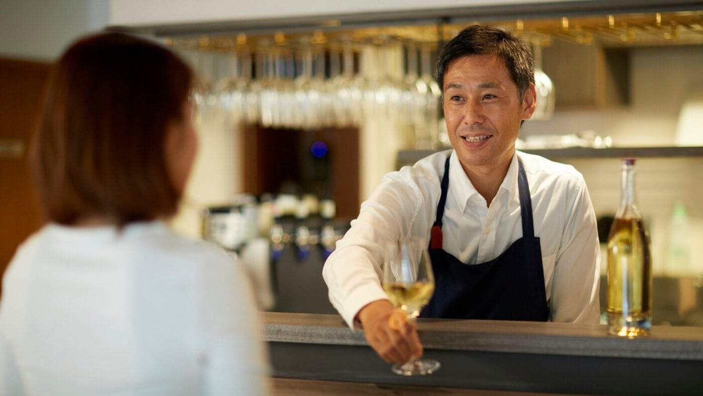 A hotel bartender serves non-alcoholic white wine to a guest.