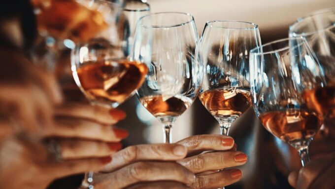Multiple wine glasses filled with white wine are raised up together.