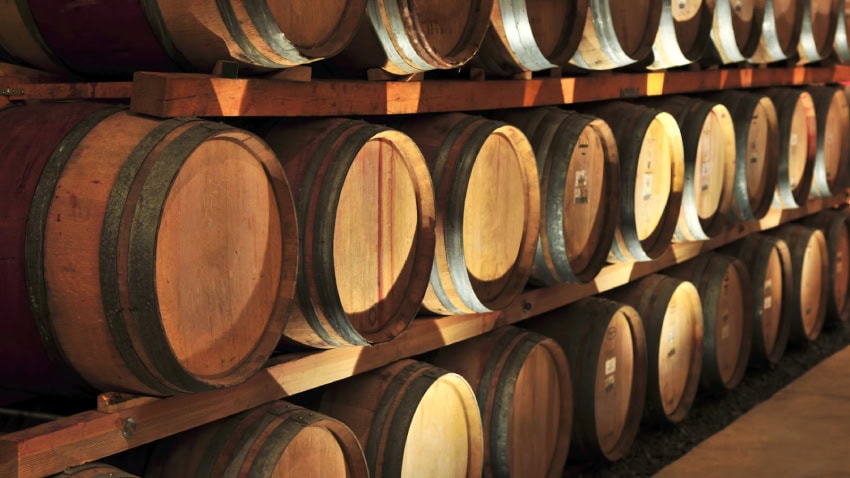 Rows of stacked oak barrels of aging wine in a winery cellar.