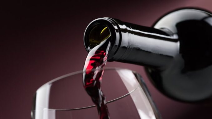 A close-up image of the rim of a wine glass as red wine is poured into it.