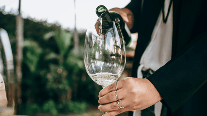 A large wine glass with light colored non-alcoholic sparkling wine being poured into it.