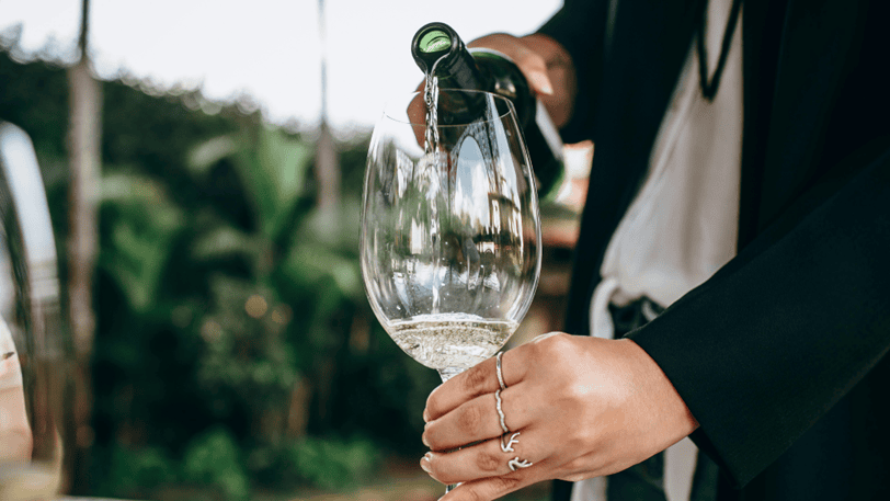 A large wine glass with light colored non-alcoholic sparkling wine being poured into it.