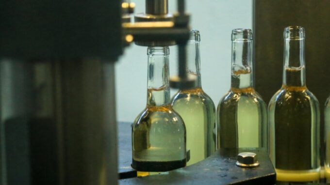 Bottles of white wine in a production line being corked and sealed.