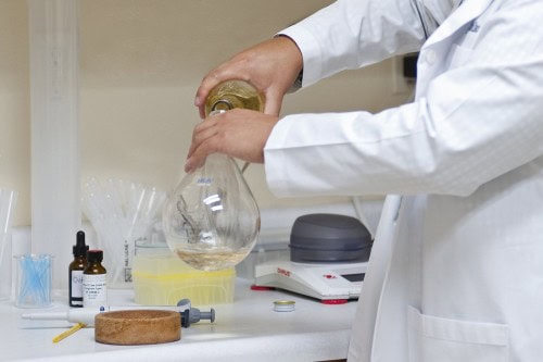 A laboratory technician in a white lab coat pours white wine into a flask for testing.